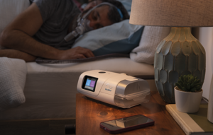 An AirCurve 11 device and mobile phone on a bedside table, with the device user sleeping in bed wearing a mask.