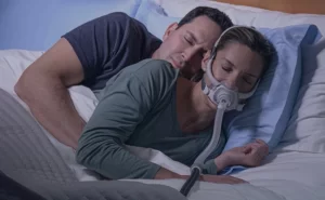 A couple sleeping cuddled together in bed, with the woman wearing an AirFit F40 CPAP mask.