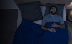 A man lying on his back in bed, snoring