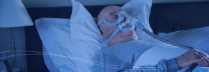 A man sleeping in bed while breathing through a ventilator.