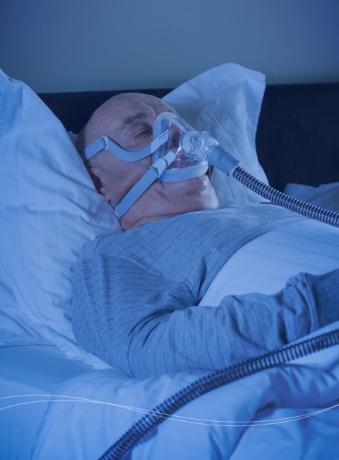 A man sleeping in bed while breathing through a ventilator.