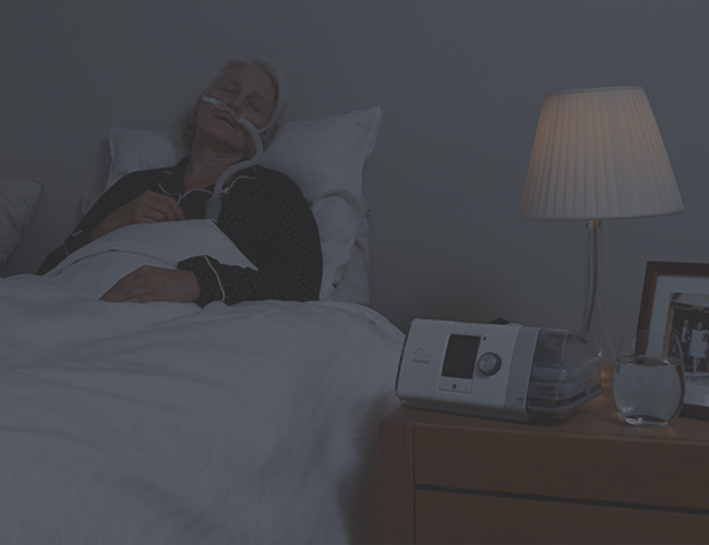 A female COPD patient sleeping in bed while wearing a Nasal Cannula connected to the Lumis HFT device