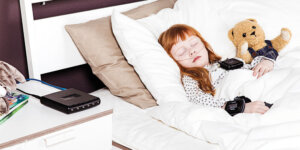 A young girl sleeping with her teddy while connected to the Nox-C1s access point device.