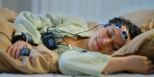 A woman sleeping peacefully while connected to the Nox SAS polysomnography device via electrodes along her forehead.