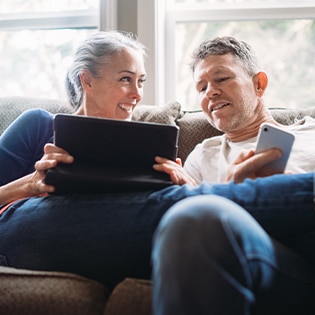 A couple sitting on the sofa with a laptop, shopping for CPAP accessories at the ResMed online shop.