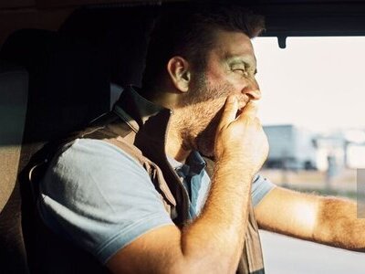 A man yawning while at the wheel of a car, illustrating a risk of sleep apnoea tiredness.