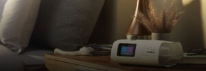 A ResMed Air11 device on a bedside table next to a lamp and some dried flowers.
