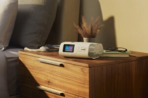 An AirCurve 11 BIPAP device, mask and mobile phone showing the myAir app on a bedside table