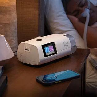 The AirCurve 11 ASV PaceWave machine shown on a bedside table as its user sleeps, with a mobile phone beside it.