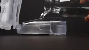 A still from a CPAP humidification video showing a humidifier tub being filled with water, overlaid with a play arrow.