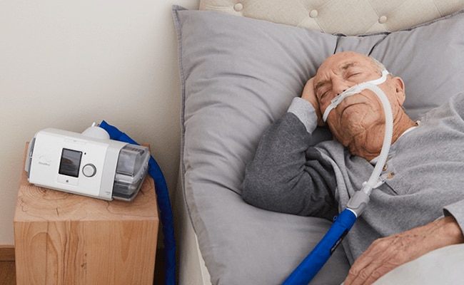 A man asleep in bed receiving high-flow –therapy from the ResMed Lumis device.
