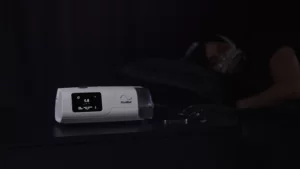 A still from a Ramp feature demonstration video showing a CPAP machine on a bedside table at night, overlaid with a play arrow.