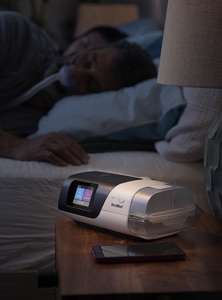 A sleep apnoea patient sleeping with an AirSense 11 CPAP-machine on the bedside table.